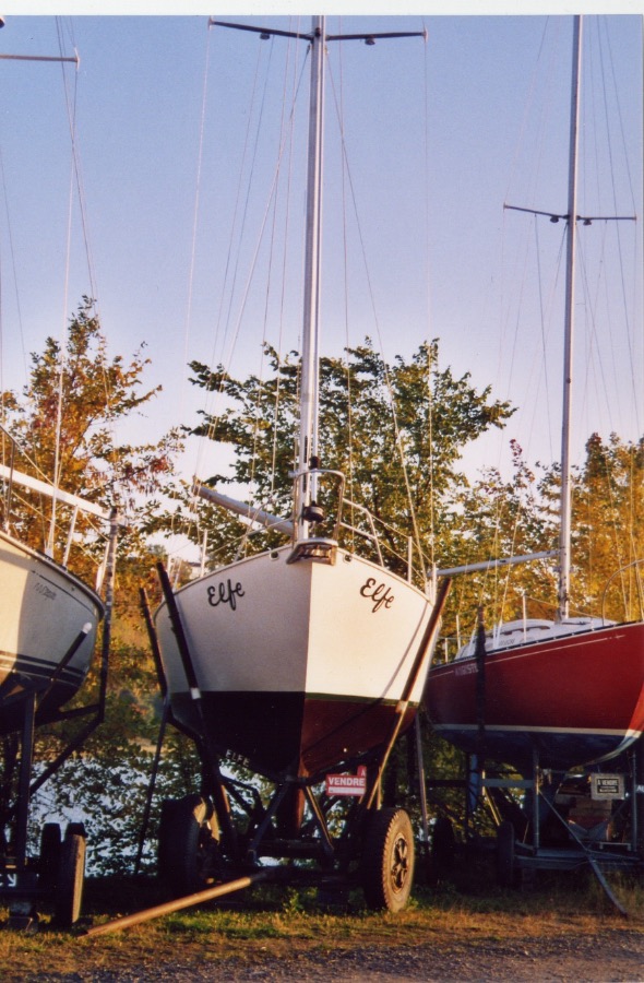 L'étrave d'Elfe, le nom peint à la main de chaque côté, le voilier sur son ber dans un chantier de la région de Québec, lumière d'automne.