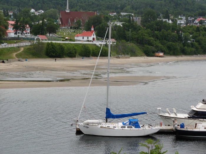 Elfe au mouillage devant un village du Saguenay, église et plage en arrière-plan.